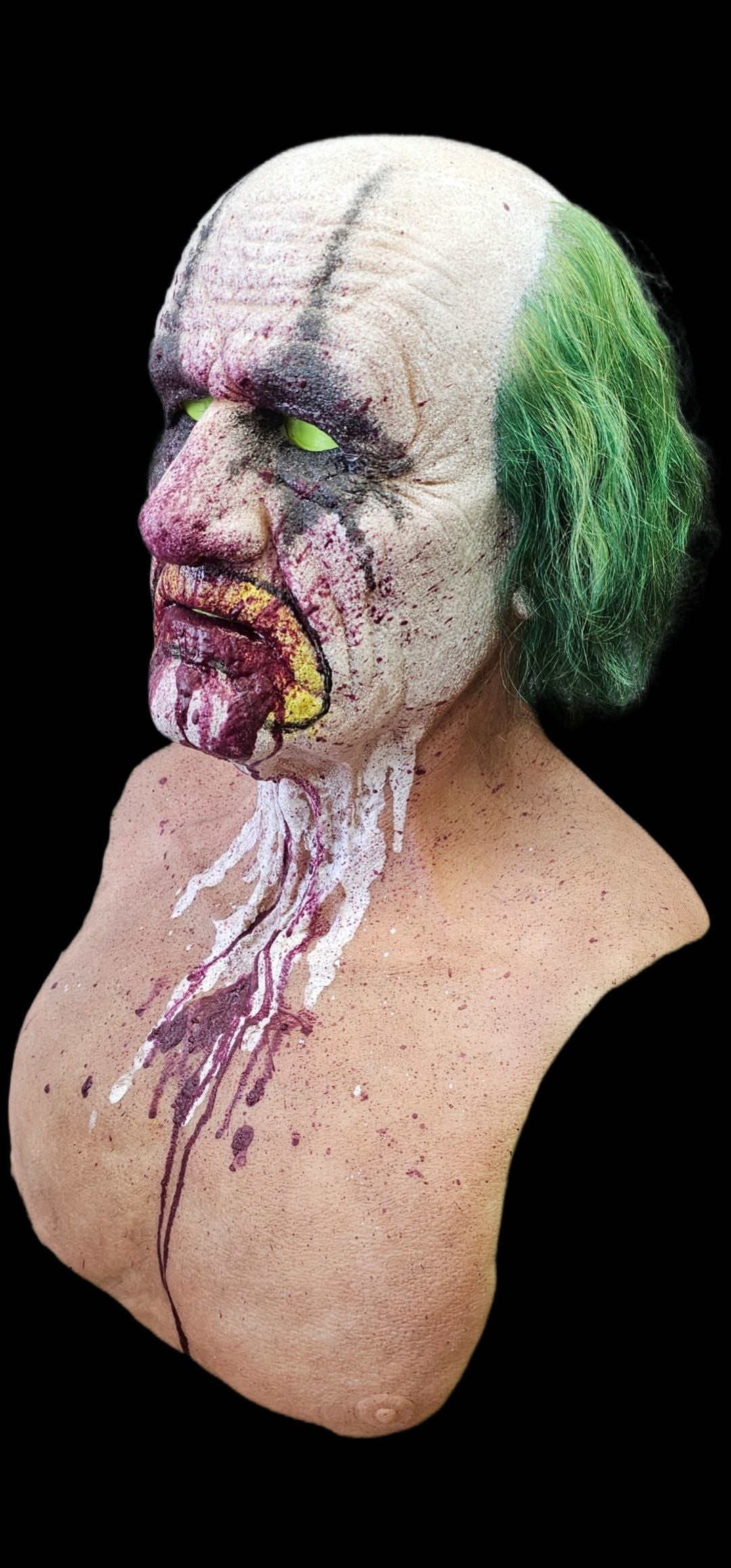 Realistic silicone mask of elder with a painted menacing bloody clown face and green hair.